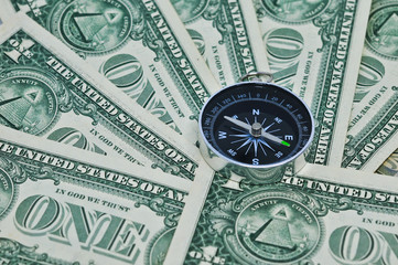 Compass laying on a pile of on dollar bills