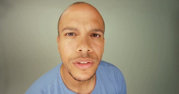 4K Attractive mixed race man looking quizzically into camera lens against a plain background