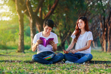 young couple reading a book and listening music with earphones in park