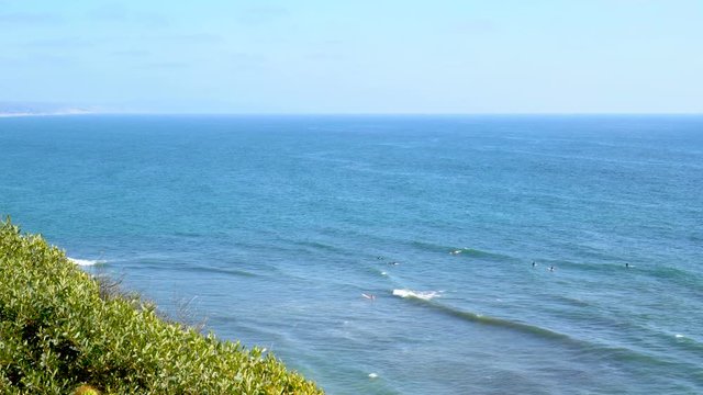 4K cliff side view of Encinitas Swami's beach in Southern California. Surfers swimming and riding waves.
