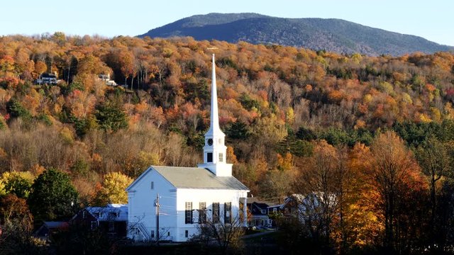 panning shot of a white new england church with a hillside covered in fall foliage at stowe in vermont, usa
