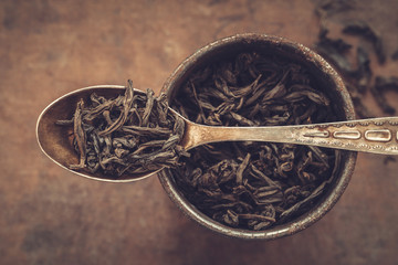 Vintage metal cup of dry tea leaves and spoon. Top view.