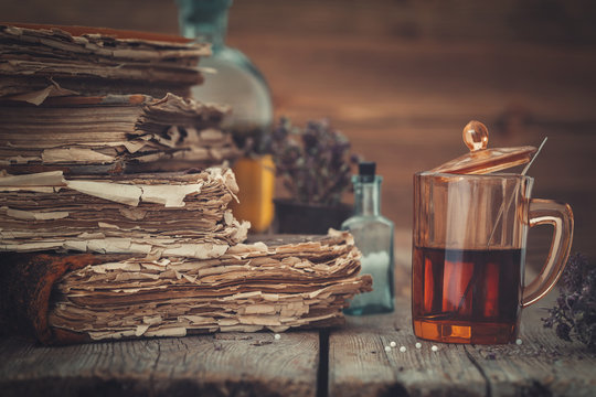 Old books, tincture or healthy tea in glass, vial of homeopathic globules and medicinal herbs.