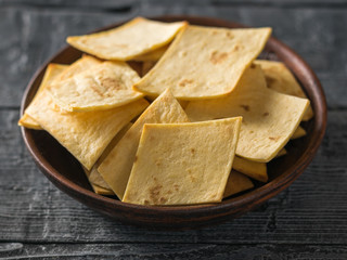 Mexican tortilla chips with cheese in a clay bowl on a rustic wooden table.