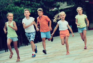 Fototapeta premium Group of cheerful children running together in town on summer
