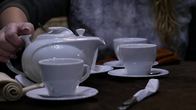 Woman pours herbal tea in a white cup in cafee. slow motion