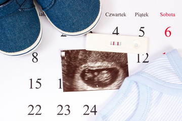 Pregnancy test, ultrasound scan of baby and clothing for newborn on calendar