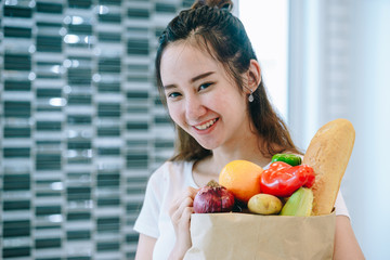 Asian woman holding the fruits in paper bag in her kitchen at her sweet home to making the dinner.