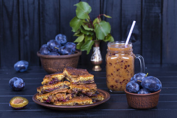 Homemade plum pie in plate, plum smoothies and raw blue plums on black wooden background,