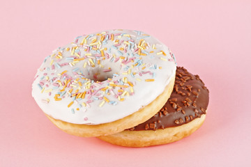 Two glazed donuts on pink background
