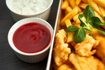 chicken nuggets with french fries and different sauces on wooden board,