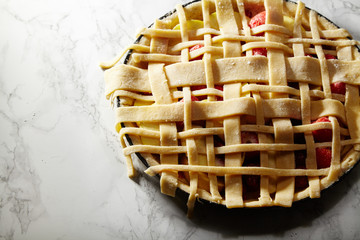 Obraz premium Uncooked pie with berries and apples decorated with beautiful piecrust lattice and leaves on white marble table at the kitchen