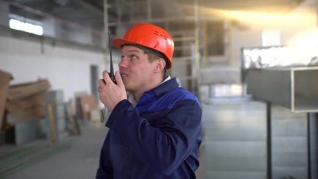 Engineer builder using a walkie talkie giving instructions at a construction site inside. 4 k