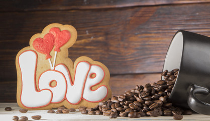 Black cup with coffee seeds, cookies in the shape of the word love and two red hearts, on a wooden background