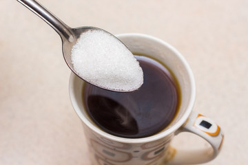  cup of coffee and  spoonful of sugar, sugar is poured into coffee