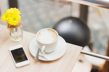 Cup of cappuccino, phone and bouquet of yellow flowers