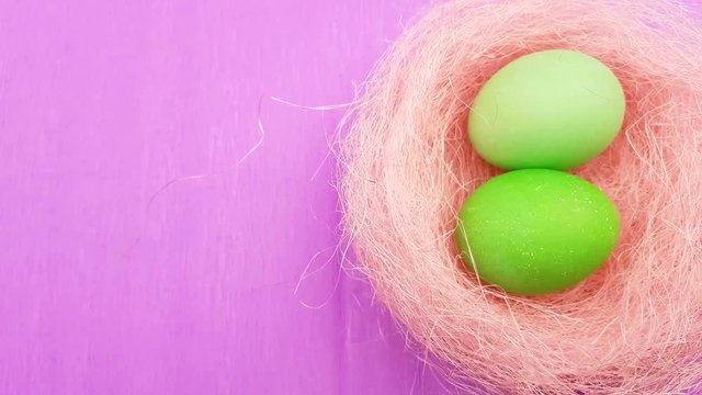 Color easter eggs in pastel pink nest on purple background.