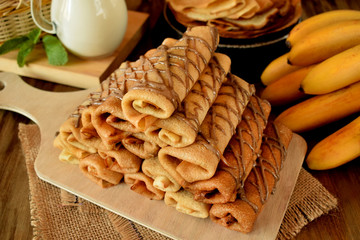 Pile of rolled crepes with banana filling on a wooden board