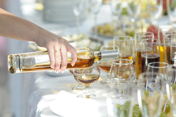 In a restaurant. Waitress’s hand pouring cognac in wineglass from a bottle 