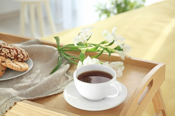 Tray with tasty breakfast and flowers on bed, closeup