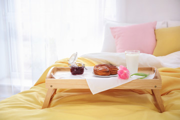 Fototapeta na wymiar Tray with tasty breakfast and tulip on bed