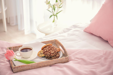 Tray with tasty breakfast and tulip on bed