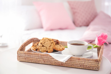 Tray with tasty breakfast and tulip on bed
