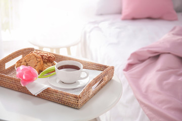 Tray with tasty breakfast and tulip on bed