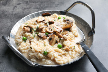 Dish with delicious risotto and mushrooms on grey background