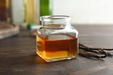 Jar with vanilla extract and sticks on wooden table