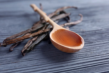 Spoon with vanilla extract and sticks on wooden background