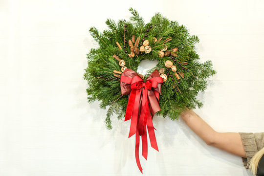 Female florist with Christmas wreath on light wall background