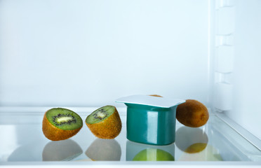 Plastic cup with yogurt and kiwi in refrigerator