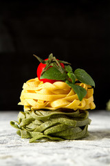 Homemade italian tagliatelle with flour, cherry tomatoes and basil. Dark background.