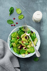 Salad of spinach baby leaves, watercress, kiwi, avocado and pomegranate in old ceramic plate on gray concrete background. Selective focus. Top view. Copy space.