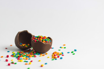 Broken Chocolate Easter egg with multi-colored candy decorations on a white background. Copy space