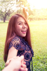 Young woman walking and hold hands her boyfriend on grass field.