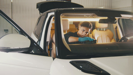 Young woman in blue gloves is cleaning interior of the car for luxury SUV