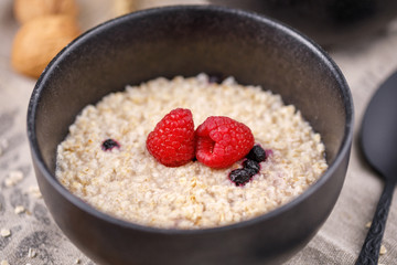 Still life with oatmeal and fresh raspberries in a refined bowl. Useful breakfast.