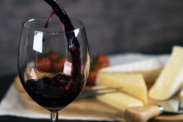 Pouring red wine into the glass against wooden background