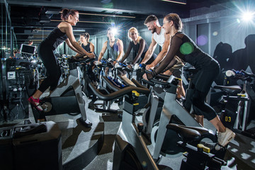 Naklejka na ściany i meble Group of sporty people training on exercise bikes together at gym.