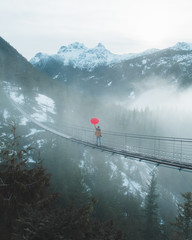 Red Umbrella on Misty Suspension Bridge in Mountains