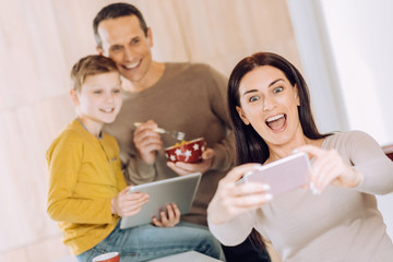 Obraz na płótnie Canvas Love my boys. Upbeat young woman taking a selfie of herself and her husband and son while they having breakfast and watching something on tablet