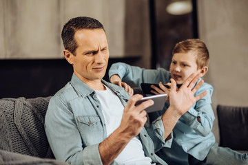 Lack of attention. Irritated pre-teen boy squeezing his fathers shoulder and trying to make him pay...