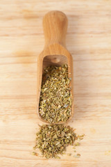 Dry Oregano herb in wood scoop on wood background.