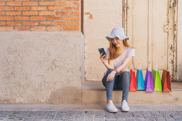 Portrait of a young hipster girl dressed in stylish clothes holding mobile phone while resting after shopping in summer day.	