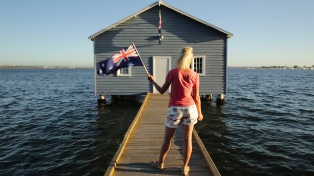 Blue Boat House: iconic most photographed Perth location in Western Australia. Popular landmark Crawley Edge Boats with wooden jetty on Swan River at sunset sky with blonde model and Australian flag.