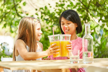 Zwei Mädchen stoßen mit Orangensaft an