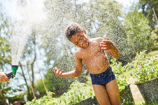 Afrikanischer Junge duscht unter Gartenschlauch