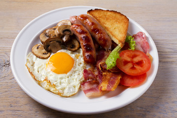 Full English or Irish breakfast: sausages, bacon, egg, mushrooms, tomatoes and toasts. Nutritious morning meal